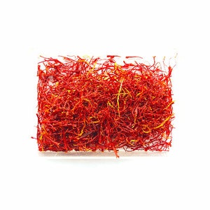 May include: A close-up of a pile of dried saffron threads in a clear plastic container. The threads are a vibrant red-orange color.