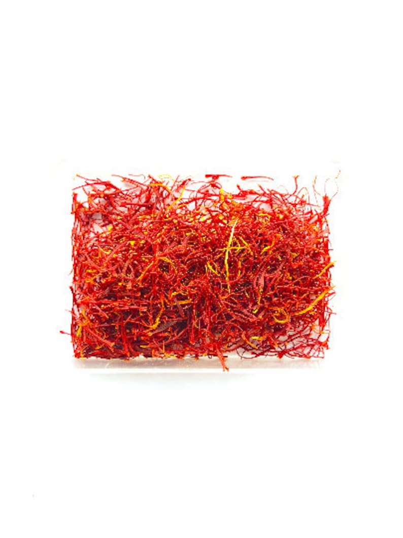 May include: A close-up of a pile of dried saffron threads in a clear plastic container. The threads are a vibrant red-orange color.