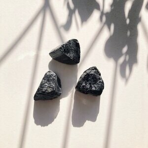 May include: Three black, rough-hewn, triangular-shaped stones. The stones are arranged in a triangular pattern on a white surface.