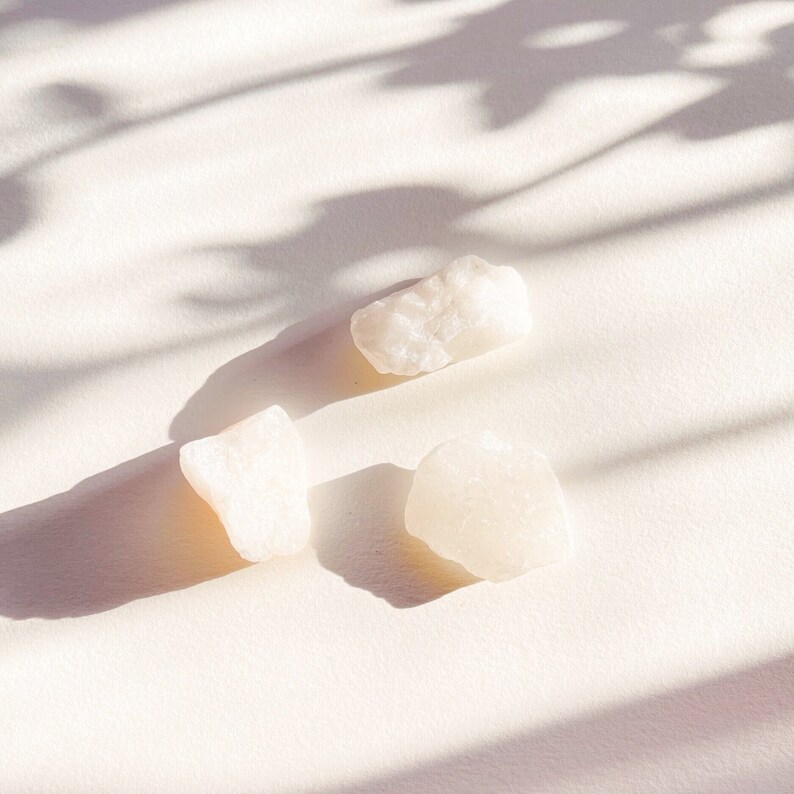 May include: Three white, opaque, irregularly shaped stones on a white background. The stones are smooth and have a slightly translucent quality.
