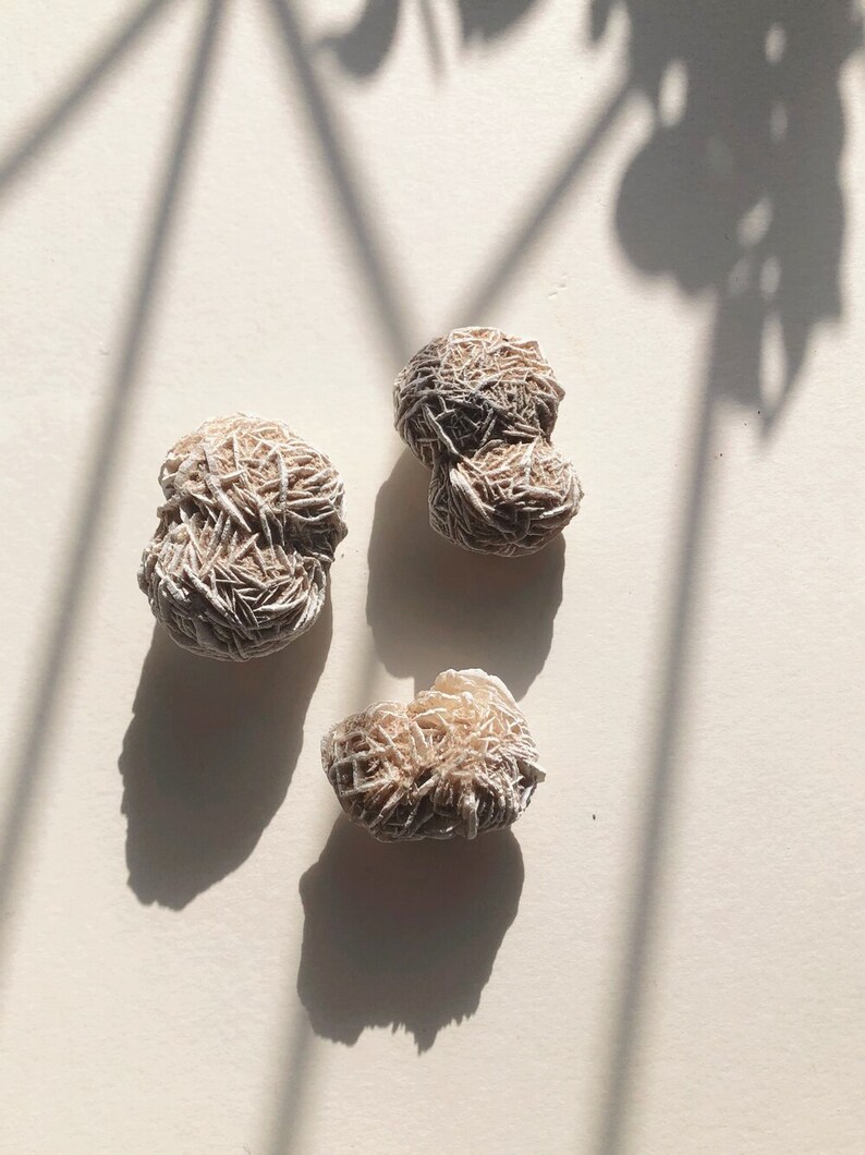 May include: Three tan-colored selenite rose quartz crystals on a white background. The crystals are arranged in a triangular pattern.