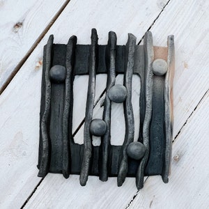 May include: Black ceramic wall art with a rectangular frame and a grid of raised lines. The frame is decorated with small, round, grey stones.