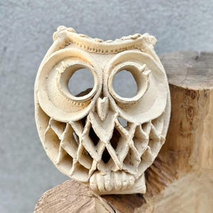 Puede incluir: Una escultura de búho de cerámica blanca con detalles intrincados, que incluyen un patrón de celosía en el pecho y grandes ojos redondos.