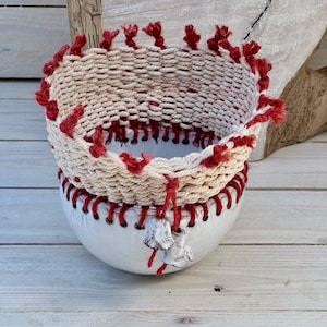 Może przedstawiać: Biała ceramiczna miska z czerwoną i białą obwódką z sznurka. Miska ma ozdobny wzór z boku i jest ozdobiona małymi białymi dzwoneczkami.