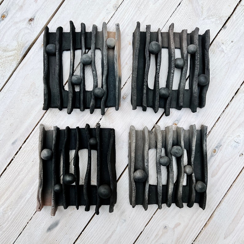 May include: Four black ceramic wall decor pieces with a wavy design and small round indentations. Each piece has a rectangular shape with a slightly raised border.