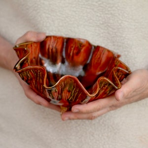 May include: A handmade ceramic bowl with a wavy, ruffled rim. The bowl is glazed in shades of brown, orange, and black, with a speckled finish.