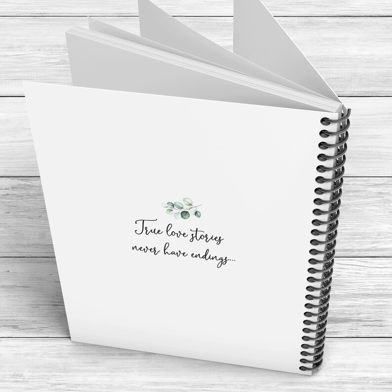 May include: A white spiral bound journal with the text "True love stories never have endings..." printed on the front cover. The text is in black cursive font and there is a small green watercolor illustration of a sprig of leaves above the text.