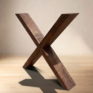 May include: A dark brown wooden table base featuring two thick, rectangular beams joined in a central X-shape. The wood displays a visible grain texture and a deep, rich finish, with the structure standing firmly on a flat, light-colored surface.
