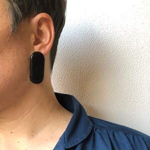 Può includere: Una persona che indossa una camicia blu scuro con un orecchino ovale nero nell'orecchio sinistro.
