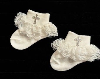 May include: A pair of white baby socks with lace trim and a rhinestone cross embellishment.