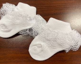 May include: A pair of white baby socks with a lace ruffle trim. The socks are made of soft cotton and are perfect for a special occasion.