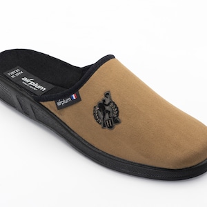 May include: A pair of brown suede slippers with a black rubber sole. The slippers feature a black embroidered logo on the top.