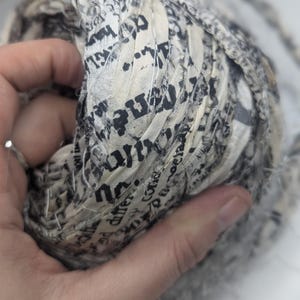 Peut inclure: Gros plan sur une boule de tissu imprim&eacute; journal. Le tissu est de couleur cr&egrave;me avec du texte noir et est &eacute;troitement enroul&eacute;. La texture semble douce et l&eacute;g&egrave;rement effiloch&eacute;e, sugg&eacute;rant un projet artisanal ou textile.