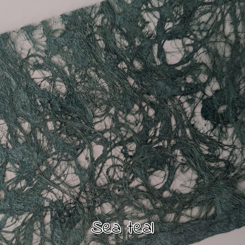 May include: Close-up of a textured paper with a sea teal color. The paper has a fibrous, interwoven appearance, with the text "Sea teal" in a white, handwritten font at the bottom.