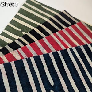 May include: Four pieces of fabric with a striped pattern in various colors. The colors include green, black, red, and navy blue, each with white stripes. The word "strata" is in the upper left corner.