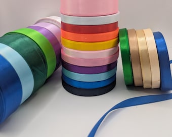 Könnte beinhalten: Eine Sammlung farbenfroher Satinbandrollen in verschiedenen Farbtönen, darunter Rosa, Weiß, Rot, Orange, Gelb und Blau. Das Bild zeigt auch Rollen aus grünem, beigem und marineblauem Band. Die Worte "Satin ribbon" sind unten geschrieben.