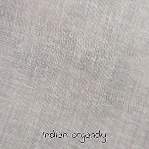 Könnte beinhalten: Nahaufnahme eines hellgrauen indischen Organdy-Stoffs. Der Stoff hat ein feines, transparentes Gewebe, das ein zartes, halbtransparentes Aussehen erzeugt. Der Text "Indian organdy" ist in kursiver Schrift am unteren Bildrand geschrieben.