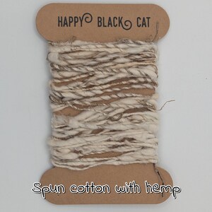 Peut inclure: Une bobine de fil de coton fil&eacute; avec des fibres de chanvre. Le fil est un m&eacute;lange de tons cr&egrave;me et marron, enroul&eacute; autour d'une bobine en carton. Le texte "HAPPY BLACK CAT" est imprim&eacute; en haut de la bobine, et "Spun cotton with hemp" en bas.