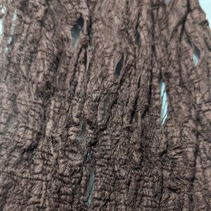 May include: Close-up of a brown, textured fabric with a rough, shredded appearance. The fabric has several holes and a crinkled texture, suggesting a distressed or aged aesthetic. The material appears to be a decorative element.