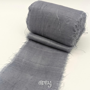 May include: A roll of grey fabric ribbon with frayed edges. The word "grey" is written in cursive at the bottom of the image. The ribbon is unspooled, revealing the texture and color of the material.