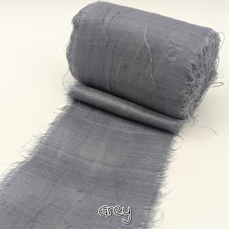 May include: A roll of grey fabric ribbon with frayed edges. The word "grey" is written in cursive at the bottom of the image. The ribbon is unspooled, revealing the texture and color of the material.