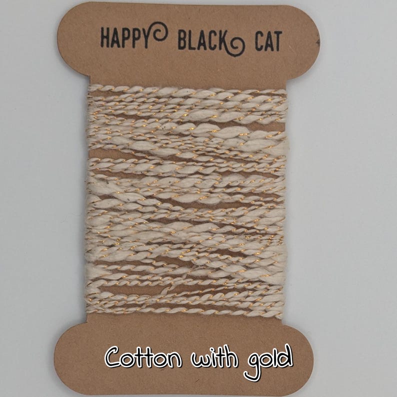 Peut inclure: Une bobine de fil de coton blanc cass&eacute; avec un fil m&eacute;tallique dor&eacute;, &eacute;tiquet&eacute;e "HAPPY BLACK CAT" et "Cotton with gold". Le fil est enroul&eacute; autour d'une bobine en carton marron, adapt&eacute; aux projets d'artisanat et de textile.