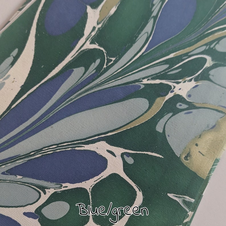 May include: A close-up of a fabric with a marbled pattern in shades of blue, green, and white. The design features flowing, organic shapes. The text "Blue/green" is written at the bottom of the image.
