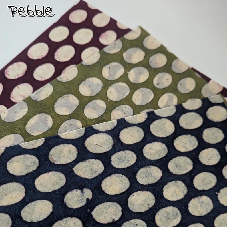 May include: Three sheets of paper with a polka dot pattern in shades of purple, green, and navy blue. The polka dots are off-white and irregularly shaped. The word "Pebble" is in the upper left corner.