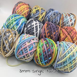 Puede incluir: Una colección de ovillos de hilo coloridos en varios tonos, incluyendo azul, amarillo, naranja y morado. El hilo está dispuesto de forma visualmente atractiva, con el texto "3mm single twist" en la parte inferior.