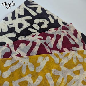 May include: Close-up of three sheets of patterned paper in black, burgundy, and yellow. Each sheet features a white, organic, abstract design. The word "Glyph" is in the upper left corner. The paper is layered, showing the different colors and patterns.