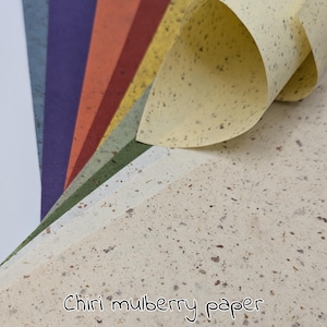May include: A stack of colorful Chiri mulberry paper sheets. The paper has a speckled texture and comes in various colors, including white, purple, orange, red, yellow, and green. The text "Chiri mulberry paper" is written at the bottom.