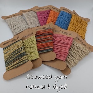 May include: A selection of spools of seaweed yarn in a range of colours, such as beige, pink, orange, blue, and yellow. Each spool has a cardboard label with the text "HAPPY BLACK CAT". The words "Seaweed yarn natural & dyed" are at the bottom.