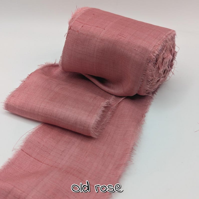 May include: A roll of old rose-colored ribbon with frayed edges. The ribbon is made of a textured fabric and is partially unrolled, revealing its width and texture. The text "old rose" is printed at the bottom.
