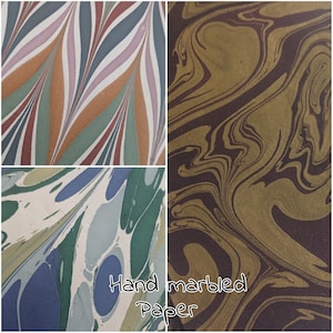 May include: A collection of three hand-marbled paper designs. One has a striped pattern in green, blue, and white. Another displays swirling gold and brown hues. The third shows blue, green, and white organic shapes. The text "Hand marbled Paper" is at the bottom.