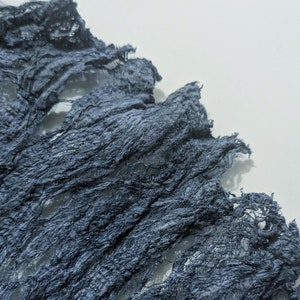 May include: Dark blue, textured fabric with a distressed appearance. The fabric has a crinkled, shredded design, creating a unique, layered effect. The material is likely used for decorative purposes, such as crafting or event decor.
