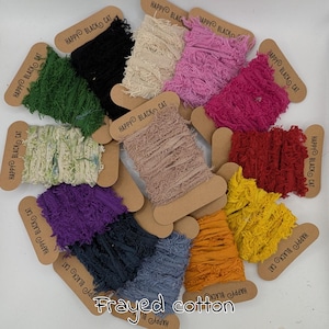 Puede incluir: Una colección de carretes de cinta de algodón deshilachada en varios colores, incluyendo negro, verde, crema, rosa, rojo, amarillo y azul. Cada carrete tiene una etiqueta de cartón con el texto "HAPPY BLACK CAT" y las palabras "Frayed cotton" en la parte inferior.