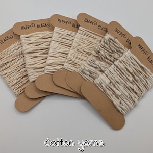 Puede incluir: Se muestran varios carretes de hilo de algodón blanquecino, cada uno unido a una etiqueta marrón con el texto "HAPPY BLACK". La imagen también incluye el texto "Cotton yarns" en cursiva.