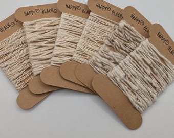 May include: Several spools of off-white cotton yarn are displayed, each attached to a brown tag with the text "HAPPY BLACK". The image also includes the text "Cotton yarns" in a cursive font.