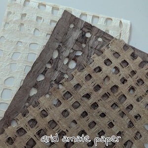 Op de afbeelding: Close-up van drie vellen grid amate papier in verschillende tinten bruin en gebroken wit. Het papier heeft een geweven textuur met een rasterachtig patroon van gaten. De tekst "grid amate paper" is zichtbaar onderaan.