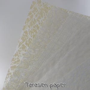 Könnte beinhalten: Ein Stapel gemusterter Papierbögen in Creme- und Weißtönen. Das oberste Blatt hat ein cremefarbenes, netzartiges Design. Das zweite Blatt weist ein Wirbelmuster auf, und das dritte hat ein lineares Design. Der Text "Tarasen paper" steht unten.