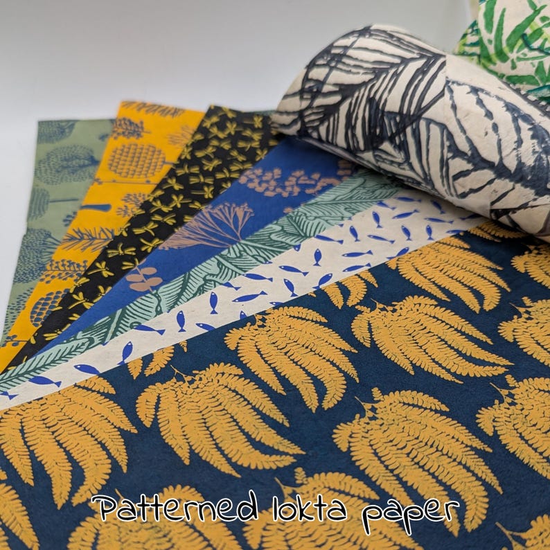 May include: A collection of patterned lokta paper sheets in various designs and colors. The patterns include ferns, leaves, and fish. Colors include navy blue, yellow, black, and green. The text "Patterned lokta paper" is visible at the bottom.