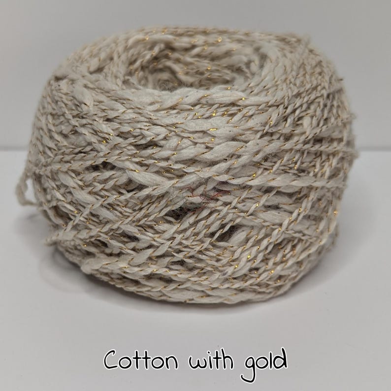 Peut inclure: Pelote de fil de coton beige avec des fils m&eacute;talliques dor&eacute;s. Le fil est &eacute;troitement enroul&eacute;, pr&eacute;sentant une surface textur&eacute;e. Le texte "Cotton with gold" est au bas de l'image.