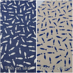 May include: Two patterned papers, one navy blue and one cream, each covered in a repeating pattern of stylized fish. The navy paper has white fish, while the cream paper has blue fish. Text at the bottom reads "Fish on blue" and "Fish on cream."
