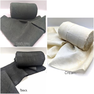 May include: Three rolls of fabric in dark grey, black, and cream colors. Each roll is partially unrolled, displaying the fabric's texture. The dark grey and black fabrics have a slightly rough appearance, while the cream fabric appears smoother.