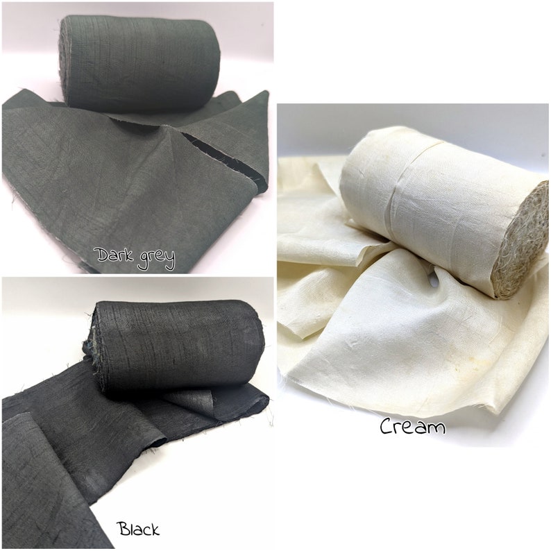May include: Three rolls of fabric in dark grey, black, and cream colors. Each roll is partially unrolled, displaying the fabric's texture. The dark grey and black fabrics have a slightly rough appearance, while the cream fabric appears smoother.