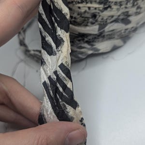 Peut inclure: Gros plan sur un ruban de tissu avec un motif z&eacute;br&eacute; noir et blanc. Le ruban est torsad&eacute;, r&eacute;v&eacute;lant sa texture et son design. Un rouleau du m&ecirc;me ruban est visible en arri&egrave;re-plan.