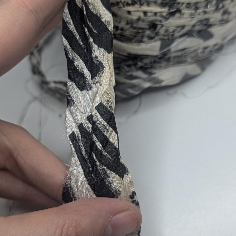 Peut inclure: Gros plan sur un ruban de tissu avec un motif z&eacute;br&eacute; noir et blanc. Le ruban est torsad&eacute;, r&eacute;v&eacute;lant sa texture et son design. Un rouleau du m&ecirc;me ruban est visible en arri&egrave;re-plan.