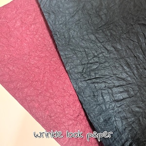 May include: Two sheets of textured paper, one in a deep rose colour and the other in a dark charcoal grey. The paper has a wrinkled appearance. The text "wrinkle look paper" is written in a cursive font at the bottom.
