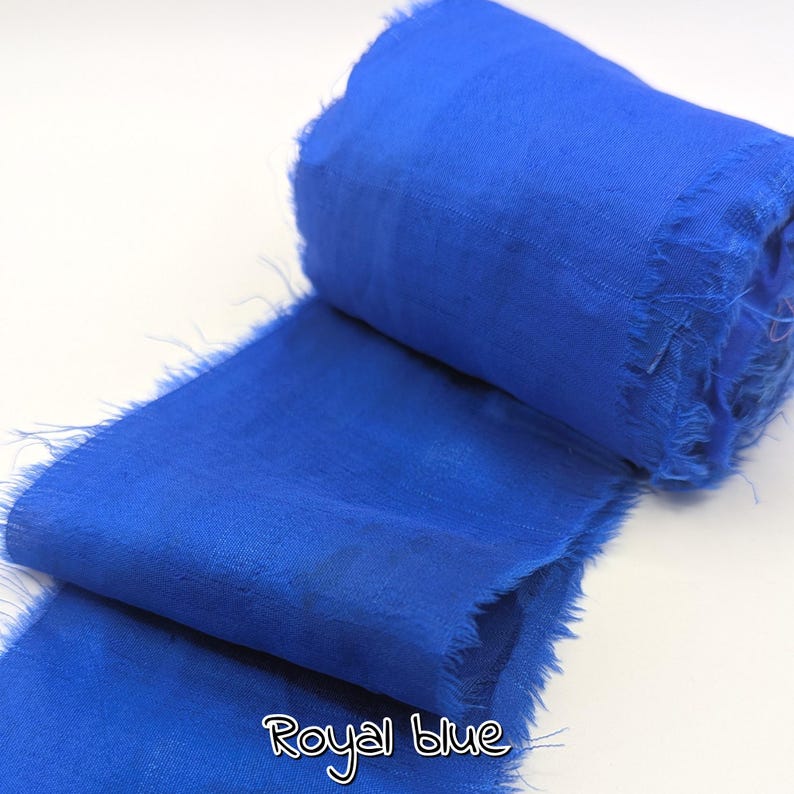 May include: A roll of royal blue fabric with frayed edges. The fabric is a vibrant shade of blue, with the words "Royal blue" written in a cursive font at the bottom. The fabric appears to be soft and lightweight.