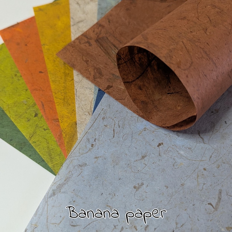 May include: A collection of handmade banana paper sheets in various colors, including green, yellow, orange, and brown. The paper has a textured appearance and is suitable for crafts and art projects. The text "Banana paper" is written at the bottom.